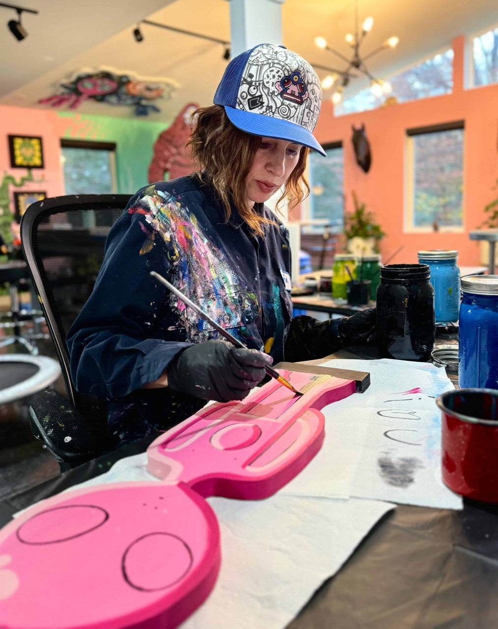 JFo painting a pink wooden alien in their studio.